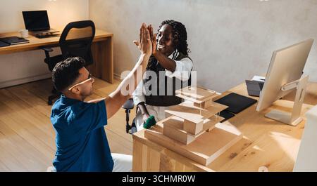 Two colleagues exchange a high-five while discussing architecture in a modern workspace. Stock Photo