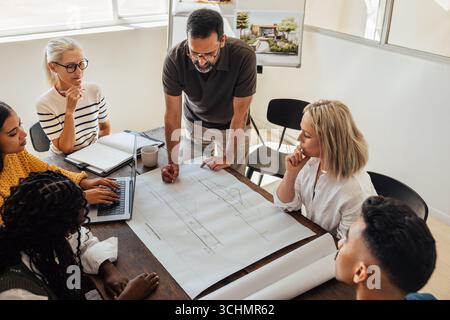 A group of professionals discussing architectural plans at a table in a bright office setting. The workspace fosters collaboration and innovation for Stock Photo