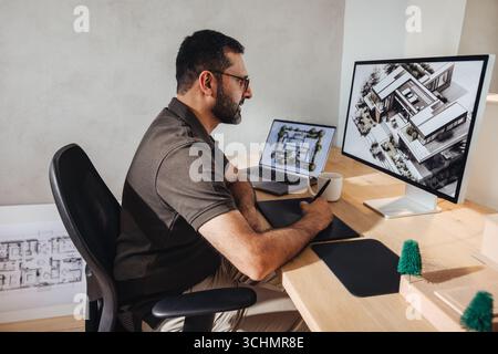 A male architect in his thirties working on an advanced building design at his desk. The workspace is modern and organized, reflecting creativity and Stock Photo