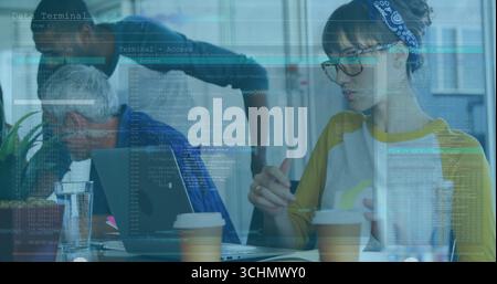 Typing Hispanic woman wearing bandana and glasses using laptop at office table, with code overlays Stock Photo