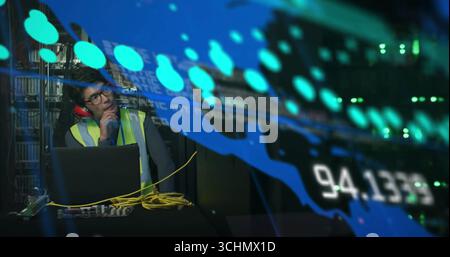 Using laptop, technician in red earmuffs and vest monitoring server data in server room, copy space Stock Photo