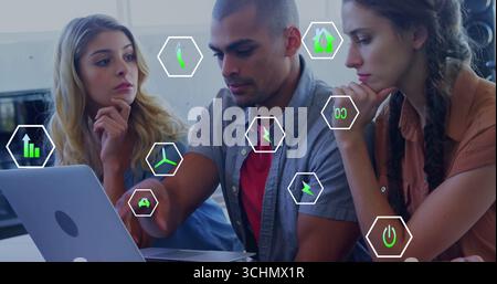 Collaborating three professionals analyzing data at office desk, with laptop and floating icons Stock Photo
