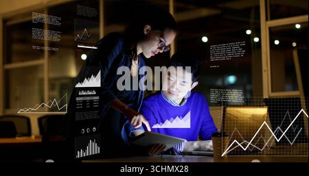 Analyzing data man and woman wearing business attire reviewing tablet and laptop in office at night Stock Photo