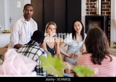 Diverse group of diverse friends enjoying conversation at home, smiling and relaxed Stock Photo