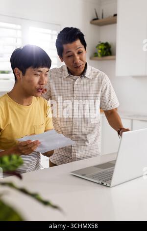 Asian father and son reviewing documents together at home using laptop Stock Photo