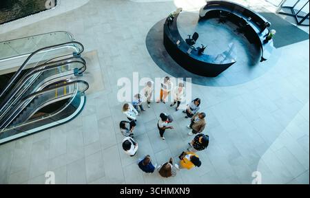 Overhead view of a corporate meeting taking place in a spacious, modern reception area. A diverse group gathers in discussion, surrounded by sleek arc Stock Photo