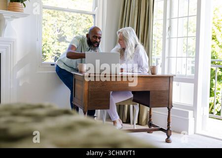 Couple planning wedding using laptop at home, discussing details and smiling Stock Photo