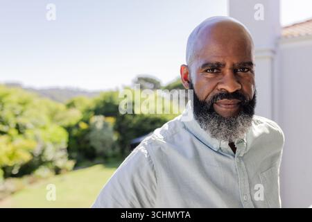 African American man standing outdoors, looking thoughtful in sunny garden setting Stock Photo