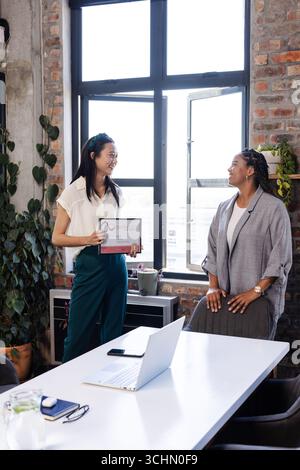 Asian woman holding certificate smiling with colleague in modern office Stock Photo