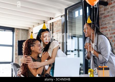 Celebrating success, diverse female colleagues in party hats and holding balloons in office, smiling Stock Photo