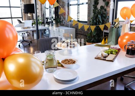 Celebrating in office with cupcakes, balloons, and snacks on table, festive mood Stock Photo