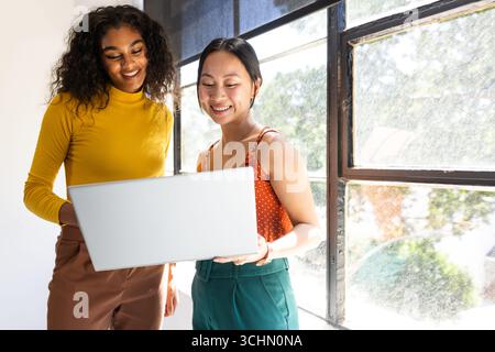 Diverse women collaborating on laptop in bright office space Stock Photo