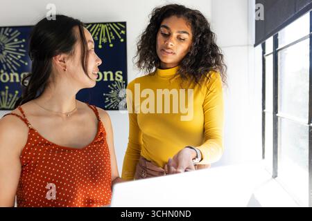 Two women collaborating on project at office, discussing ideas with focus Stock Photo