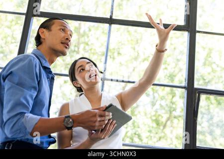 Diverse colleagues discussing project details while using tablet near large office window Stock Photo