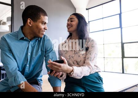 Discussing project in office, diverse colleagues holding smartphone, engaged and smiling Stock Photo