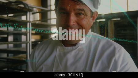 Working chef wearing white coat tall hat handling stainless rack trays in bakery with teal overlay Stock Photo