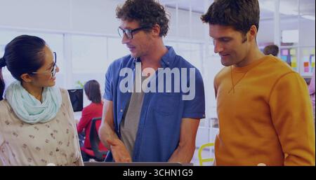 Collaborating colleagues reviewing project on laptop in open plan office, colorful sticky notes Stock Photo