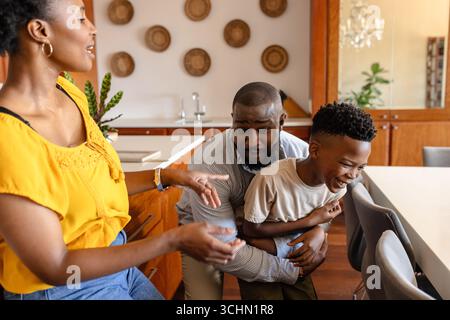 Happy family playing together in kitchen, father hugging son while mother laughs Stock Photo