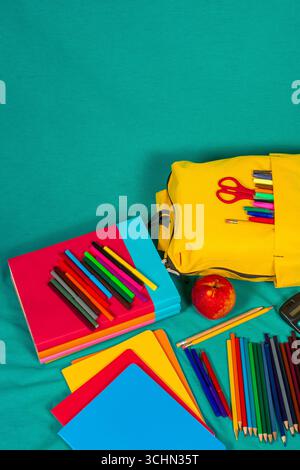 Colorful school supplies, backpack and apple resting on turquoise background Stock Photo
