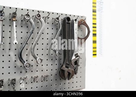 Various hand tools, including adjustable wrenches and curved box spanners, hanging on a metal pegboard organizer. Stock Photo