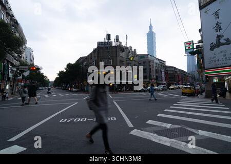 Pedestrians in motion blur cross a busy street in Taipei, with the iconic Taipei 101 tower in the background. Stock Photo