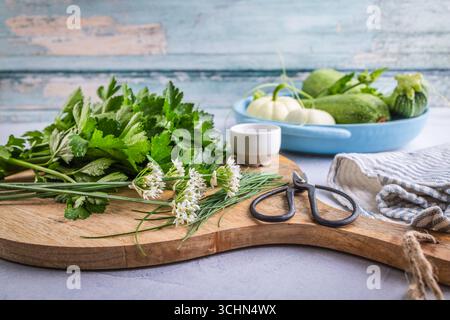 Organic green herbs, wild garlic, parsley and lovage on cutting board with zucchini in a bowl Stock Photo