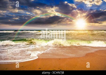 stormy beach scenery with waves splash on sand shore under scenic clouds on the sky at sunset. dark moody nature background for travel. scenic view of Stock Photo