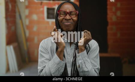 Woman holding coin with fingers crossed, african american, standing at indoor construction site, showcasing crypto enthusiasm and focusing on blockcha Stock Photo