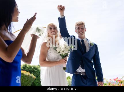 Bride and groom celebrating outdoors, holding hands and smiling joyfully Stock Photo