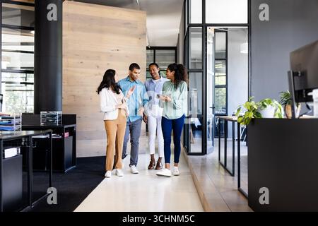 Diverse business team walking in modern office, discussing project on tablet Stock Photo