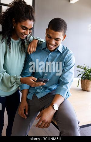 Diverse colleagues in office sharing smartphone, smiling and discussing new project ideas Stock Photo