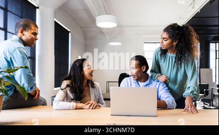 Diverse business team collaborating around laptop in modern office, discussing ideas Stock Photo