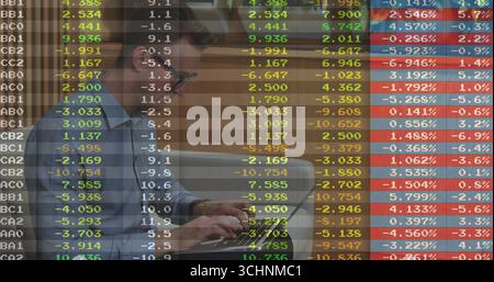 Reviewing man in light blue shirt reading financial chart overlay on laptop screen in office Stock Photo