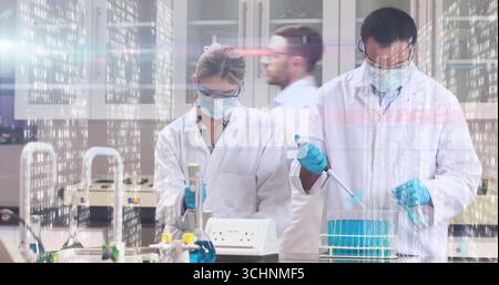 Lab scientists in coats and gloves pipetting blue solution into tube rack in lab, with micropipette Stock Photo