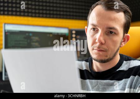 Programmer analyzing printed material with code on screens behind, conveying review and planning phase of software project Stock Photo