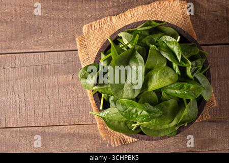 Green baby spinach leaves in wooden bowl on wooden background. Organic food concept. Stock Photo