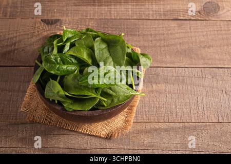 Green baby spinach leaves in wooden bowl on wooden background. Organic food concept. Stock Photo