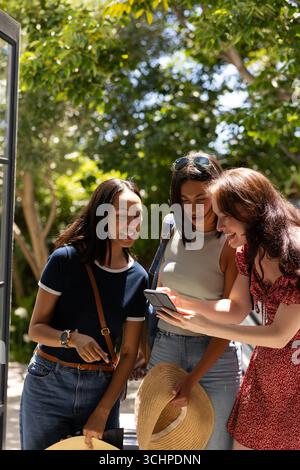 Laughing and sharing moment, three young women look at smartphone outdoors Stock Photo