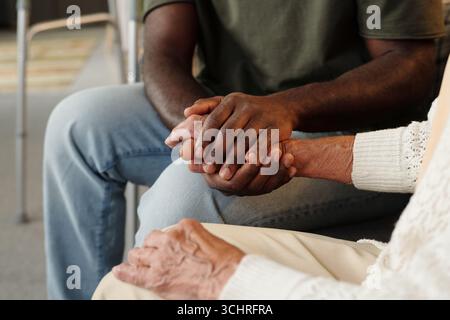 Black man holding hands with senior Caucasian woman, offering comfort and support, close up on hands showing intergenerational connection and emotional care in supportive setting Stock Photo