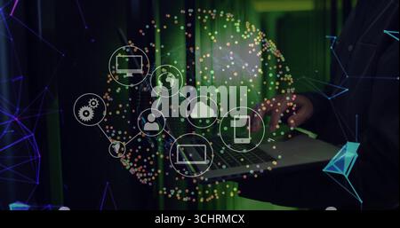 IT engineer wearing blazer typing on laptop in data center, with server racks, icons, copy space Stock Photo