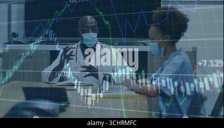 Doctor with stethoscope and mask discussing graphs while nurse types on tablet in conference room Stock Photo