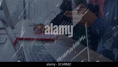 Coworkers clicking mouse on red pad and scrolling smartphone at desk, with laptops financial charts Stock Photo