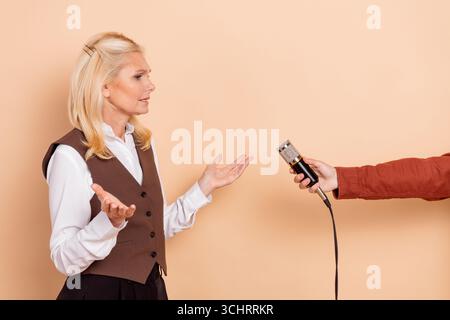 Confident mature businesswoman answering interview questions with microphone against a beige background Stock Photo