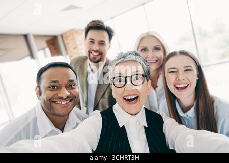 Group of diverse colleagues joyfully taking a selfie in an office setting during a team-building event Stock Photo