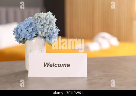 Card with word Welcome and hydrangea flowers on grey table indoors Stock Photo
