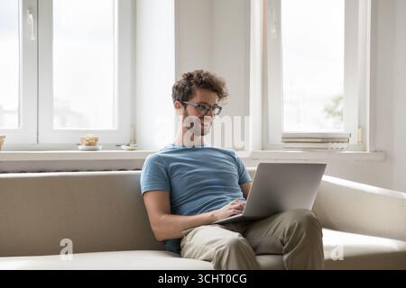 Happy millennial male sitting on cozy sofa enjoy using notebook Stock Photo