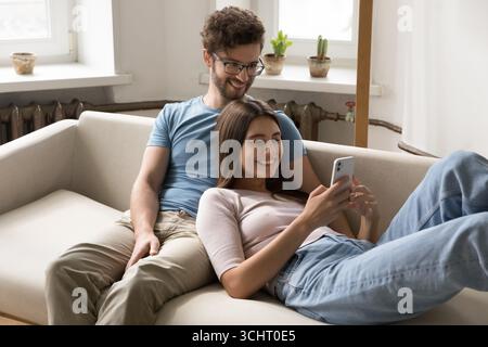Wife lounge back on husband relax on sofa using smartphone Stock Photo