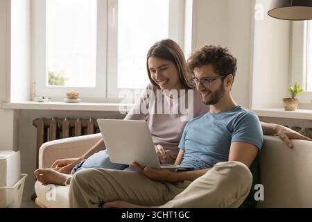Happy millennial spouses spend cozy weekend at home using notebook Stock Photo