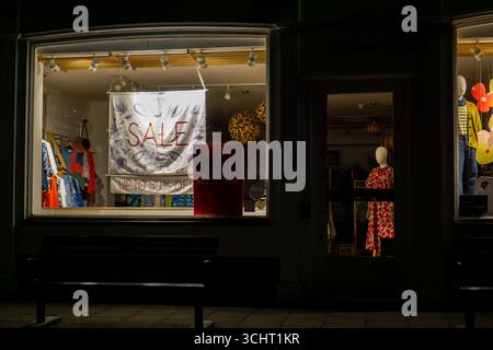 A storefront in Saffron Walden, Essex, England, at night with a 'SALE' sign in a brightly lit window. Stock Photo