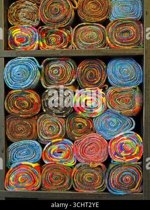 brightly coloured display of uneven rolls of knitted wool cloths stacked on wooden shelves creating colourful spiral patterns Stock Photo